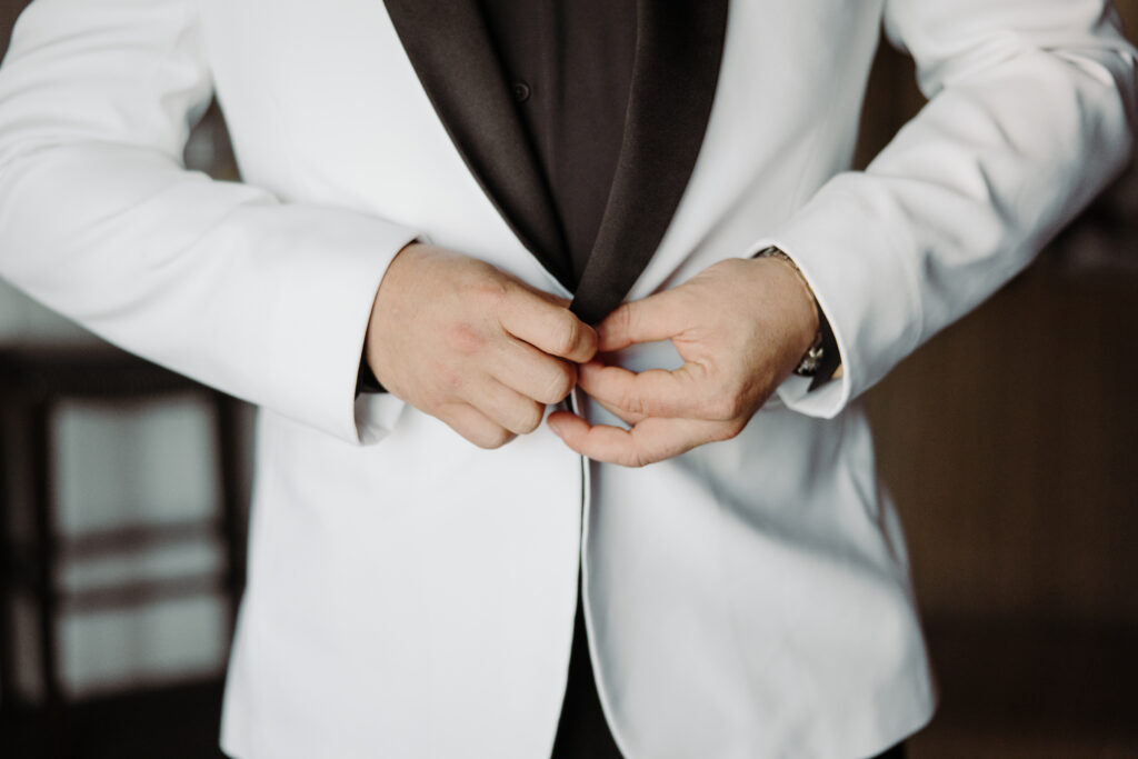 groom getting ready buttoning white jacket