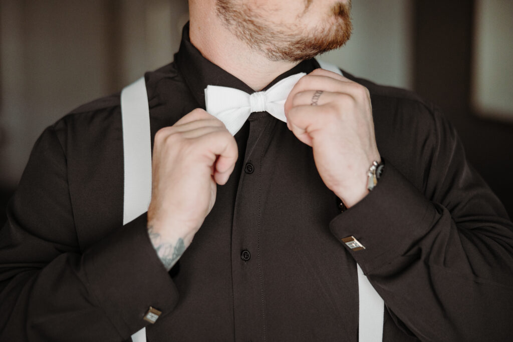 groom wearing black holding white bowtie