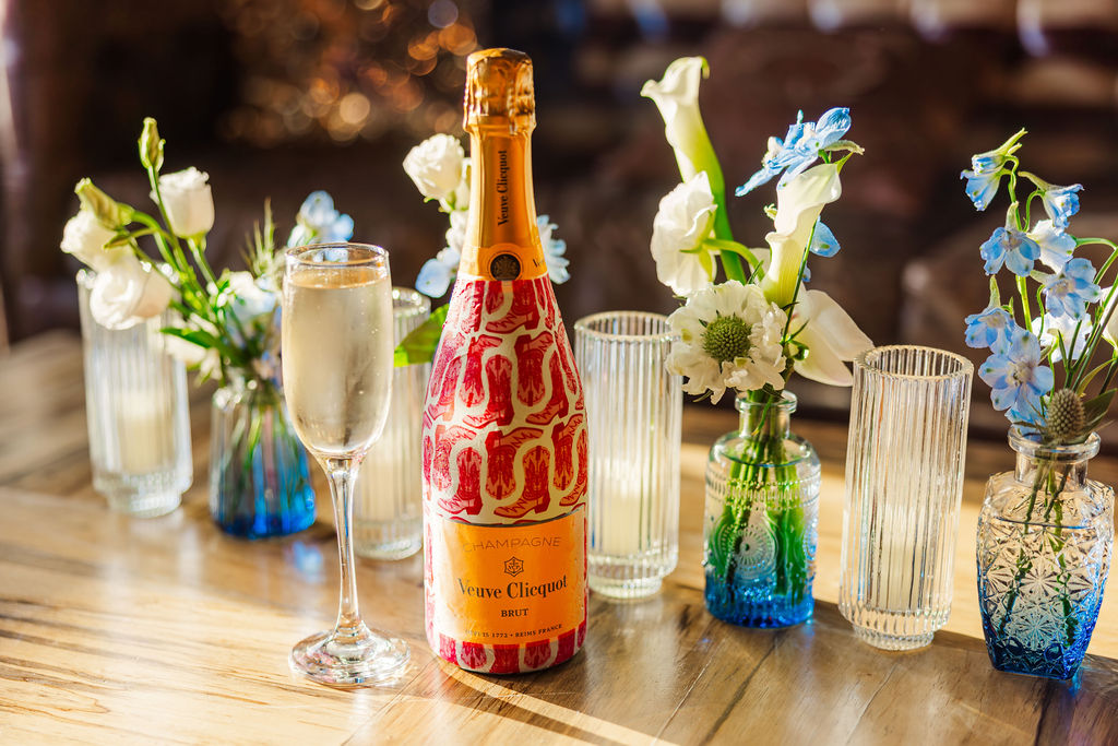 Customized bottle of champagne sitting on front of white and blue floral centerpieces