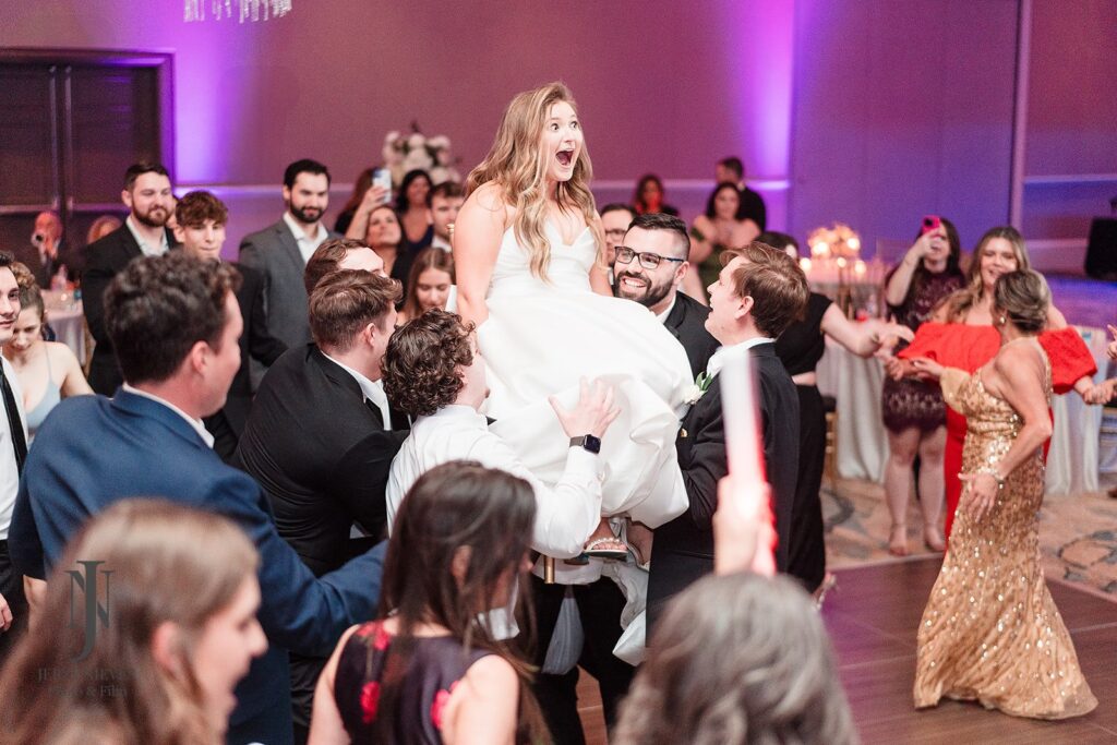 bride sitting in chair being lifted by wedding guests at reception