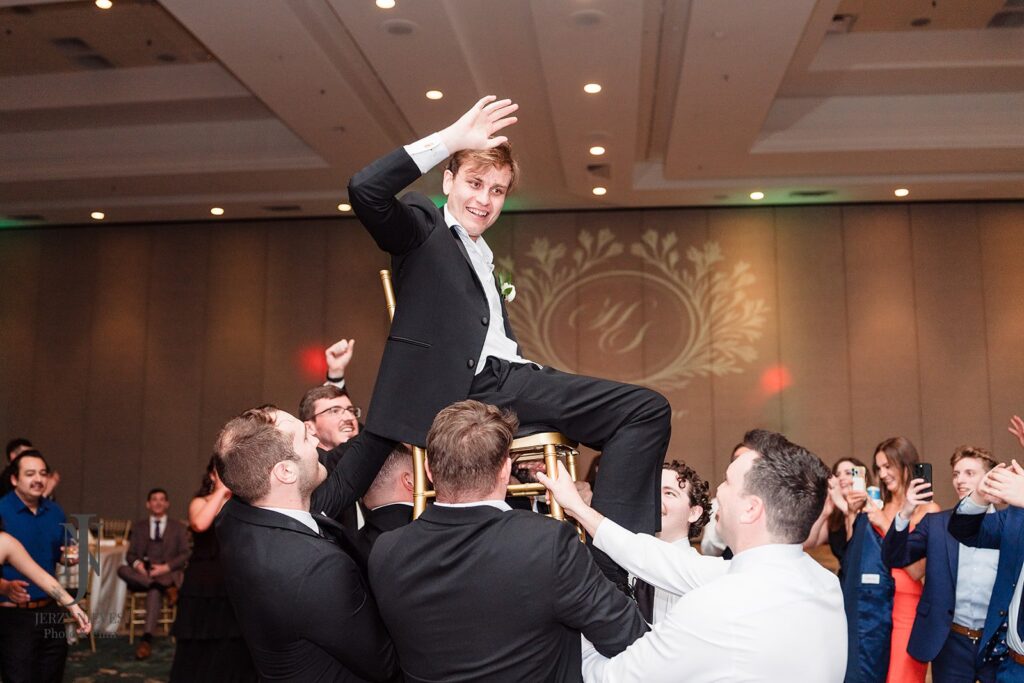 groom sitting in chair being lifted into the air by groomsmen
