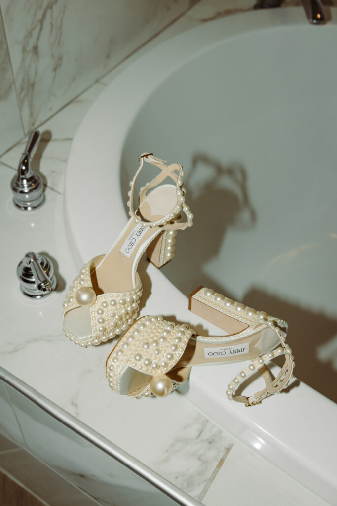 Pearl-embellished Jimmy Choo bridal heels displayed on the edge of a marble bathtub.