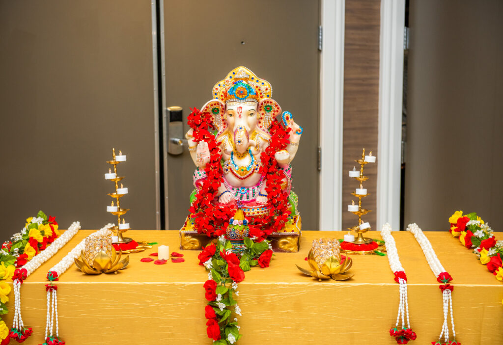 A beautifully decorated idol of Lord Ganesha adorned with red flower garlands, placed on a golden cloth-covered alter.
