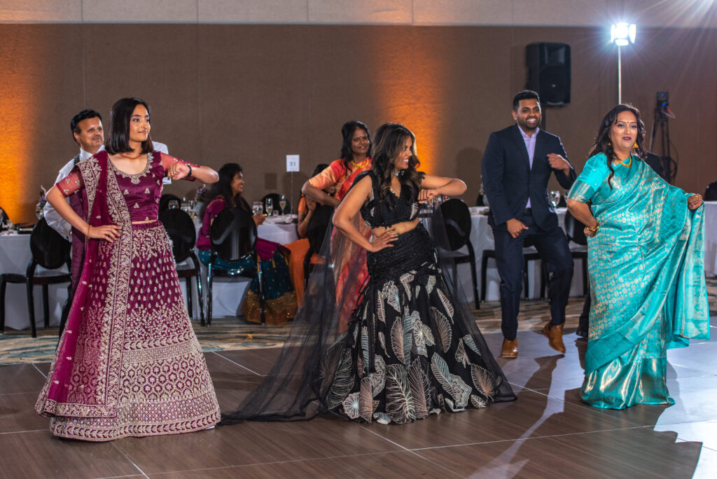 Guests in colorful traditional Indian attire performing a choreographed group dance for the bride and groom at a wedding reception.