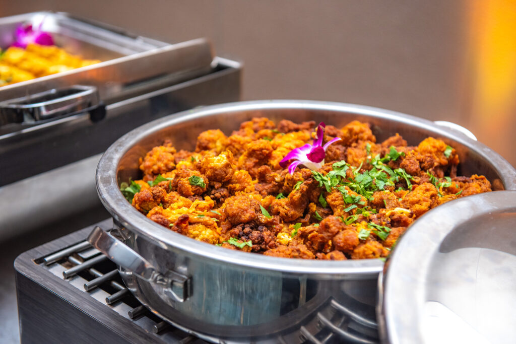 Stainless steel serving dish filled with crispy fried cauliflower florets garnished with cilantro and a purple orchid
