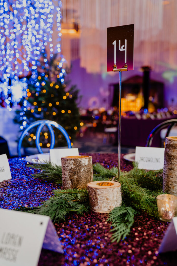 Wooden candle holders and Christmas greenery centerpieces with lit up christmas tree in the background