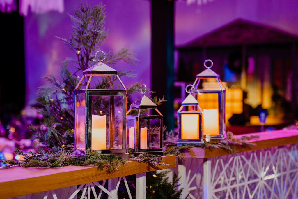 Rows of lanterns filled with faux candles seated on top of Christmas greenery